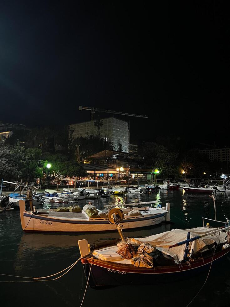 Budva, Montenegro - 25 december 2022. Fishing boats moored off the illuminated coast of the resort town at night photo