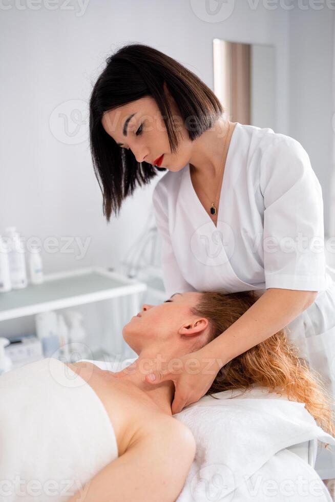 Beautician giving neck massage to woman lying on bed at beauty spa photo