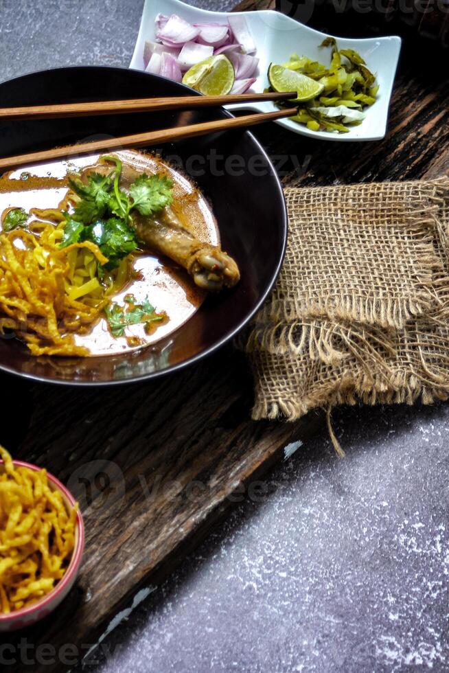 A female chef garnishing her Khao Soi Kai with a lime slide, Khao Soi Kai or Thai noodles curry with egg noodles and chicken drumstick. photo