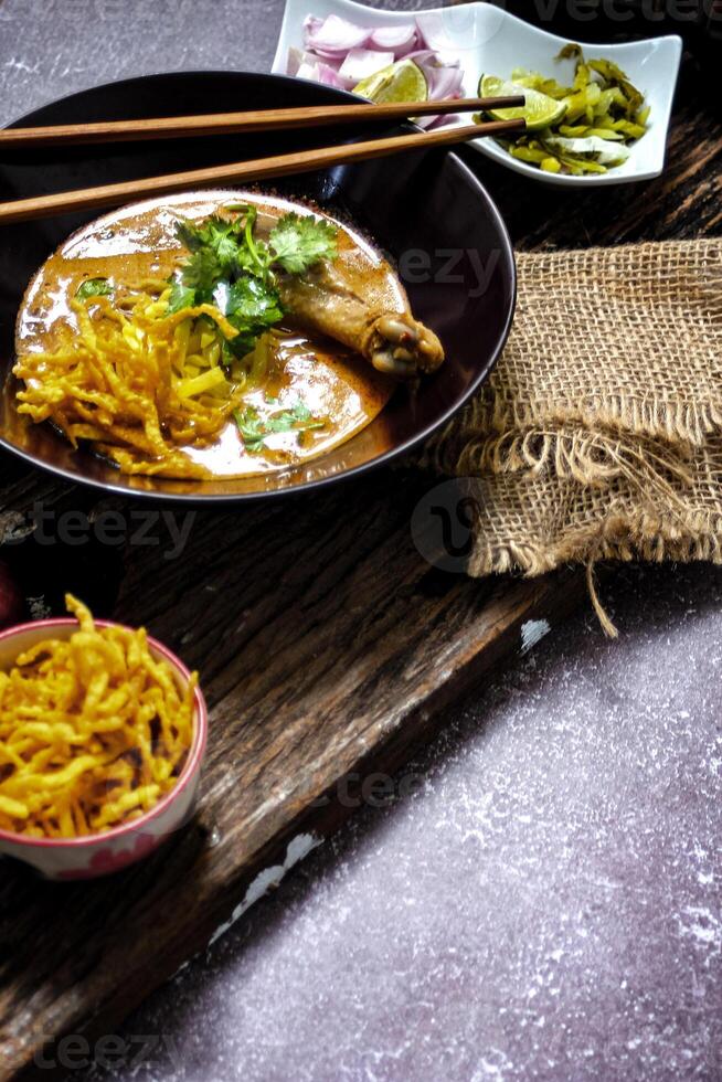 un hembra cocinero adornar su Khao asique kai con un Lima deslizar, Khao asique kai o tailandés tallarines curry con huevo tallarines y pollo palillo de tambor. foto