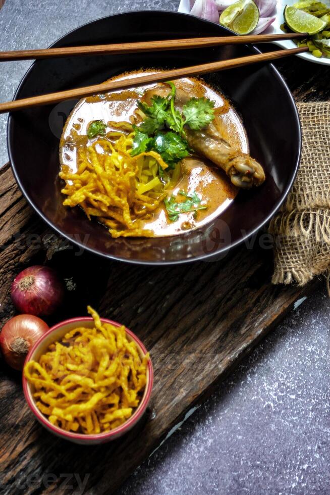 A female chef garnishing her Khao Soi Kai with a lime slide, Khao Soi Kai or Thai noodles curry with egg noodles and chicken drumstick. photo