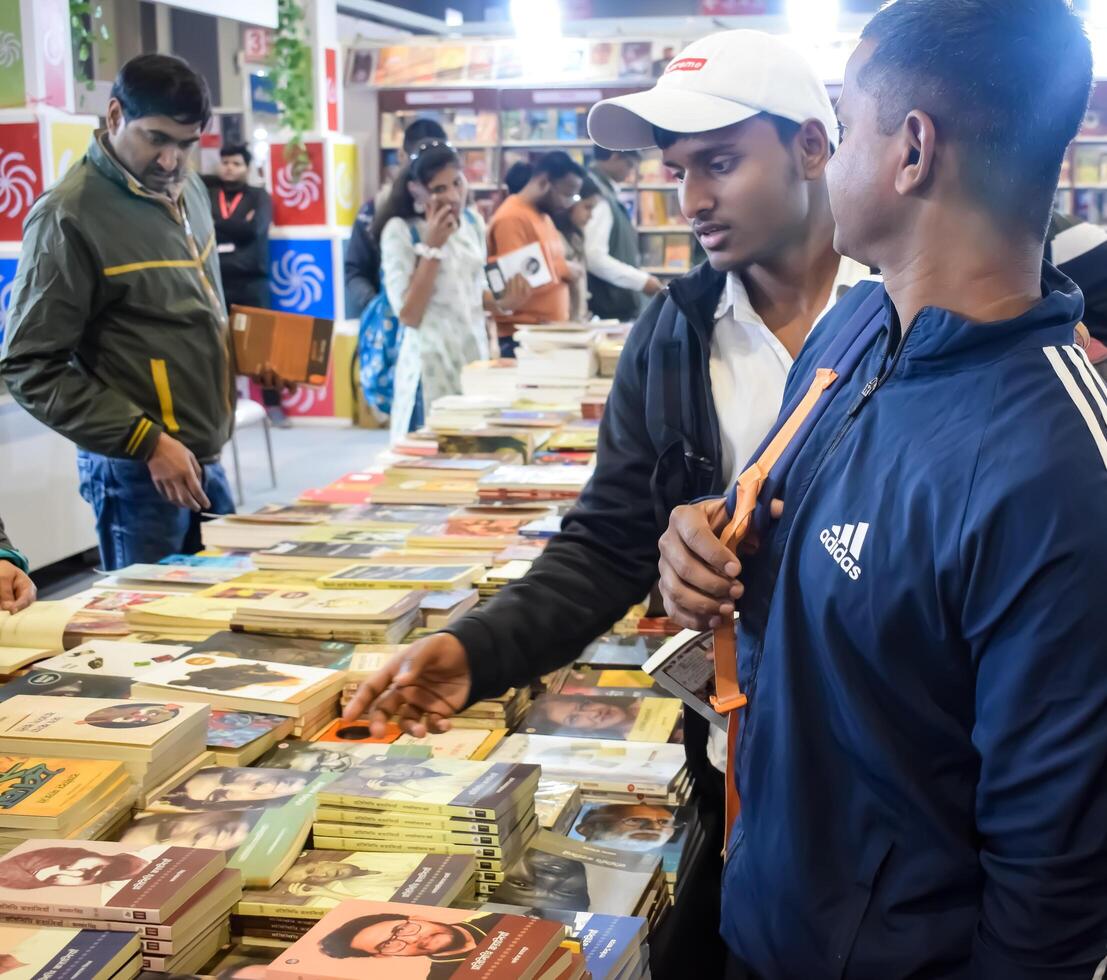 Delhi, India, February 17 2024 - Various age group people reading variety of Books on shelf inside a book-stall at Delhi International Book Fair, Books in Annual Book Fair at Bharat Mandapam complex photo