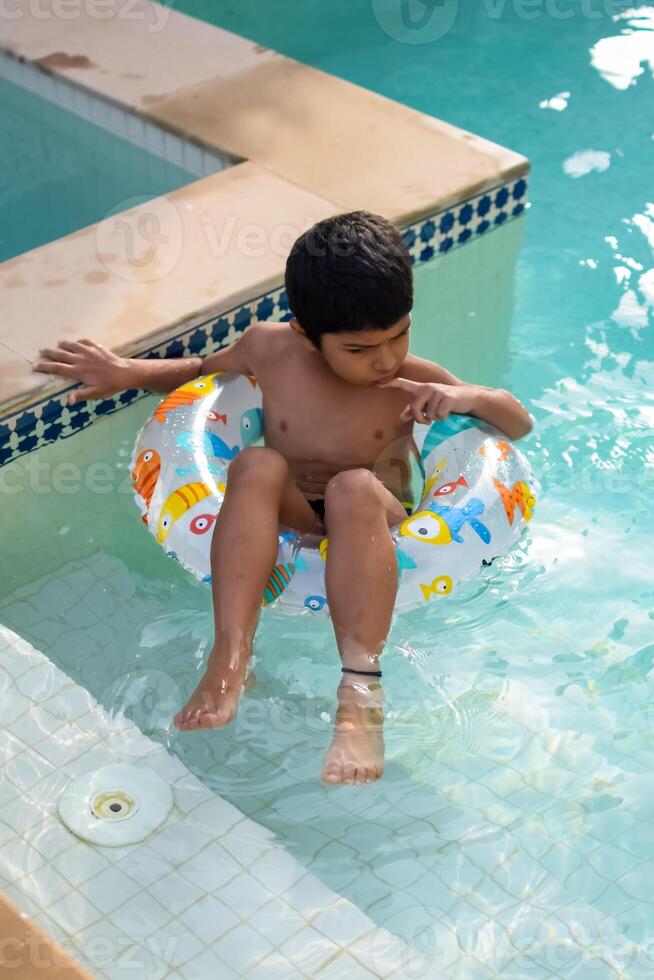 contento indio chico nadando en un piscina, niño vistiendo nadando disfraz a lo largo con aire tubo durante caliente verano vacaciones, niños chico en grande nadando piscina. foto