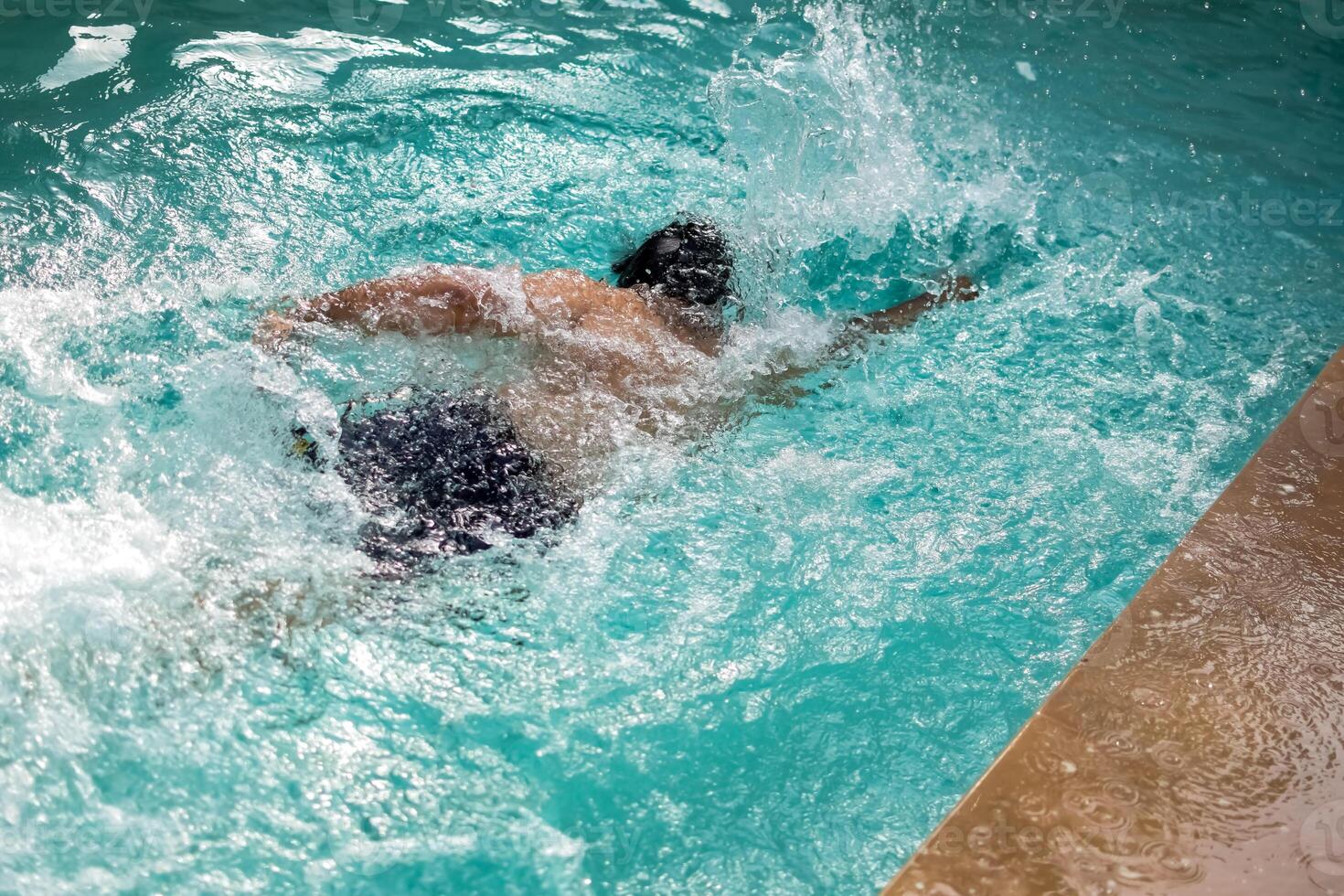 Happy Indian boy swimming in a pool, Kid wearing swimming costume along with air tube during hot summer vacations, Children boy in big swimming pool. photo