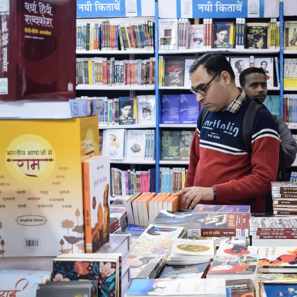 Delhi, India, February 17 2024 - Various age group people reading variety of Books on shelf inside a book-stall at Delhi International Book Fair, Books in Annual Book Fair at Bharat Mandapam complex photo