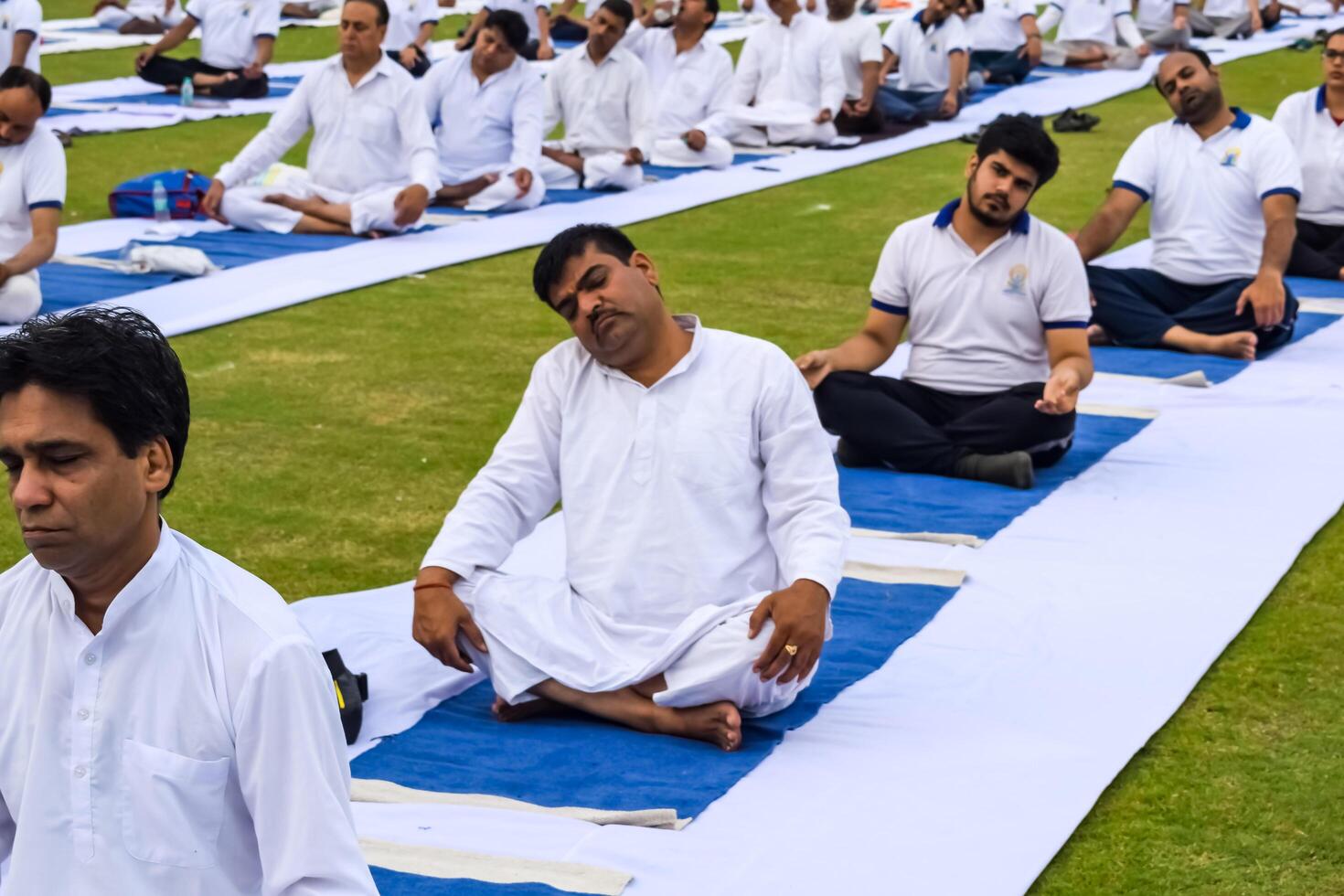 New Delhi, India, June 21, 2023 - Group Yoga exercise session for people at Yamuna Sports Complex in Delhi on International Yoga Day, Big group of adults attending yoga class in cricket stadium photo