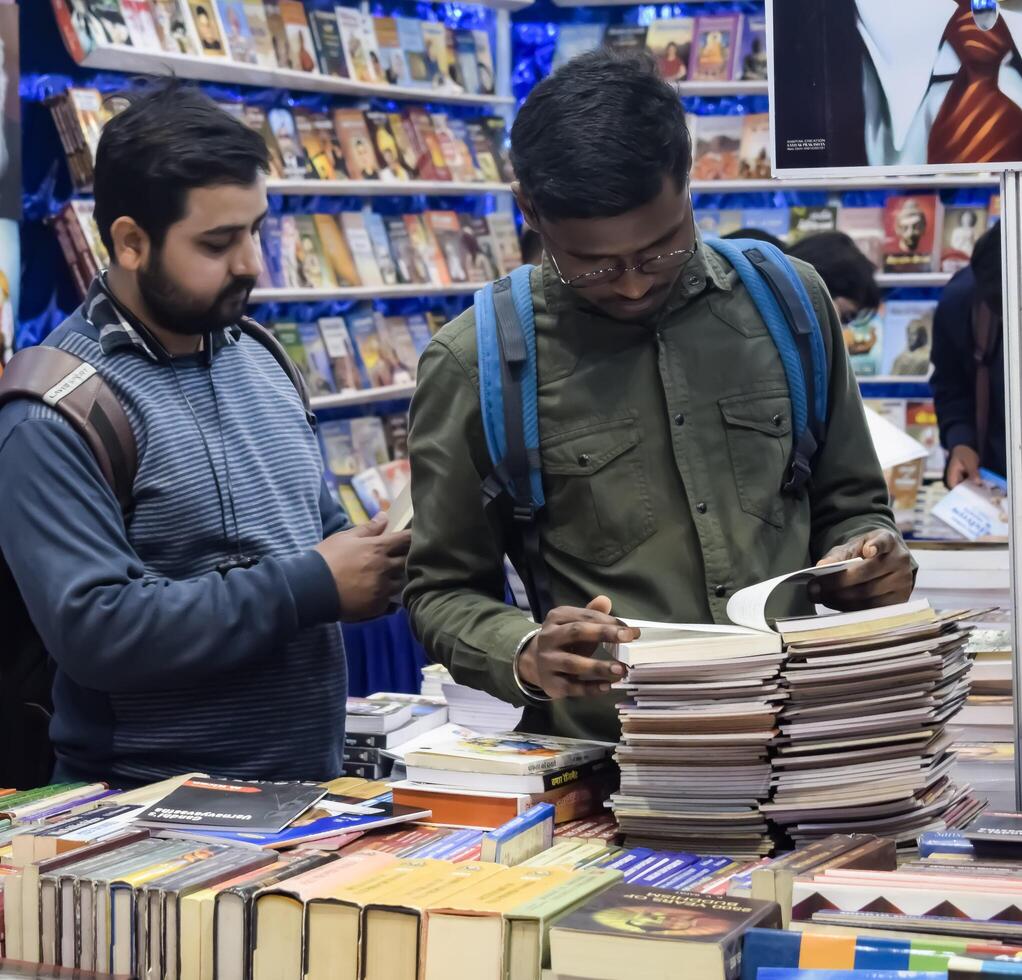 Delhi, India, February 17 2024 - Various age group people reading variety of Books on shelf inside a book-stall at Delhi International Book Fair, Books in Annual Book Fair at Bharat Mandapam complex photo