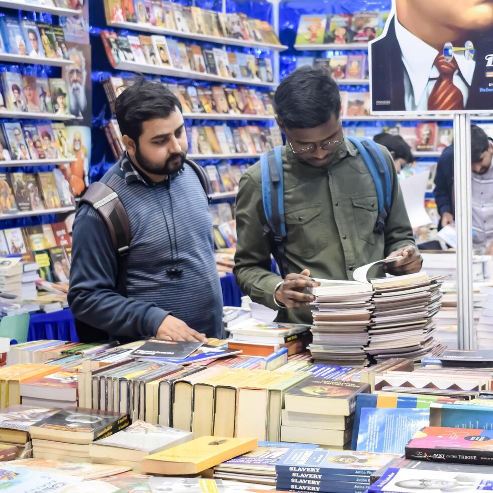 Delhi, India, February 17 2024 - Various age group people reading variety of Books on shelf inside a book-stall at Delhi International Book Fair, Books in Annual Book Fair at Bharat Mandapam complex photo