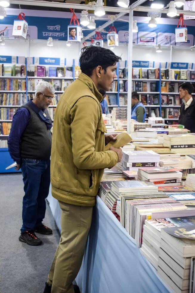 Delhi, India, February 17 2024 - Various age group people reading variety of Books on shelf inside a book-stall at Delhi International Book Fair, Books in Annual Book Fair at Bharat Mandapam complex photo