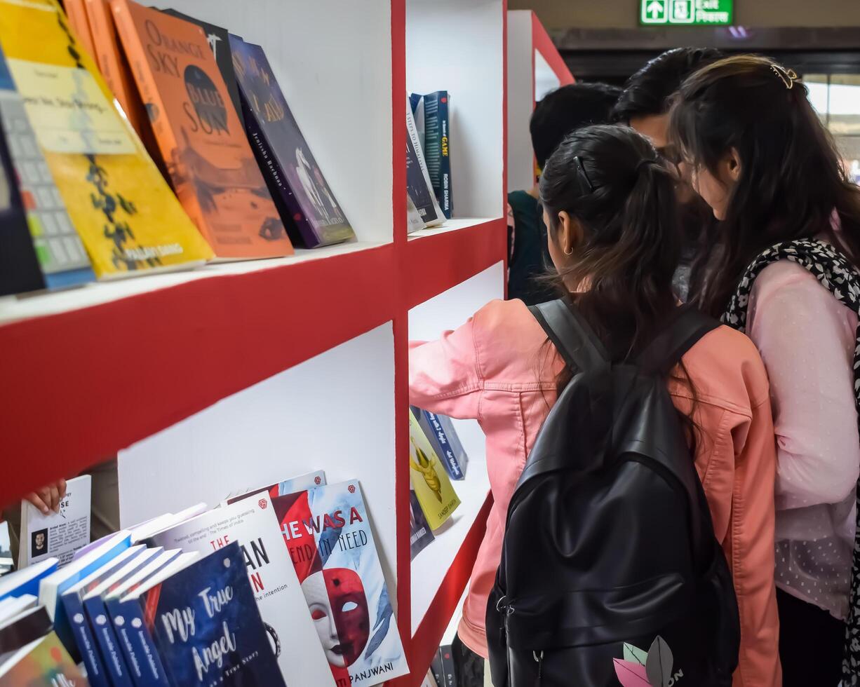 Delhi, India, February 17 2024 - Various age group people reading variety of Books on shelf inside a book-stall at Delhi International Book Fair, Books in Annual Book Fair at Bharat Mandapam complex photo