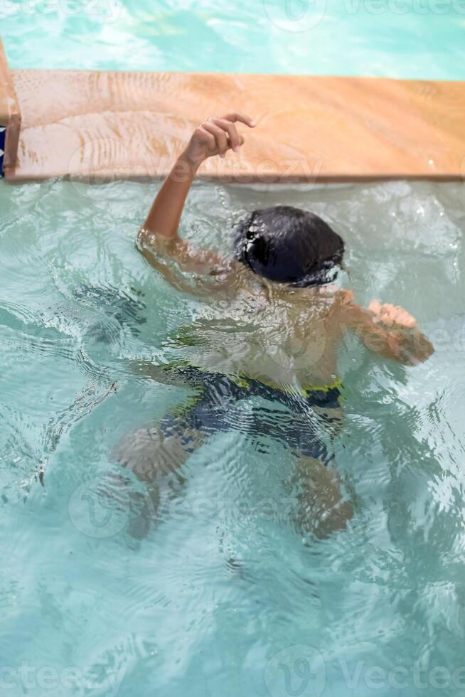 contento indio chico nadando en un piscina, niño vistiendo nadando disfraz a lo largo con aire tubo durante caliente verano vacaciones, niños chico en grande nadando piscina. foto