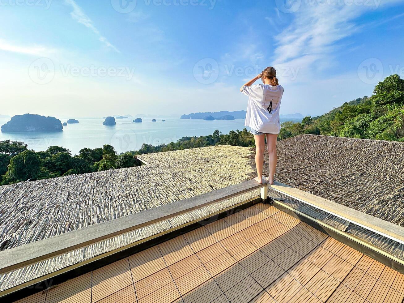 A woman enjoys a serene morning walk along a terrace with a stunning panoramic view of distant islands under a bright sun, showcasing the perfect blend of relaxation and natural beauty photo