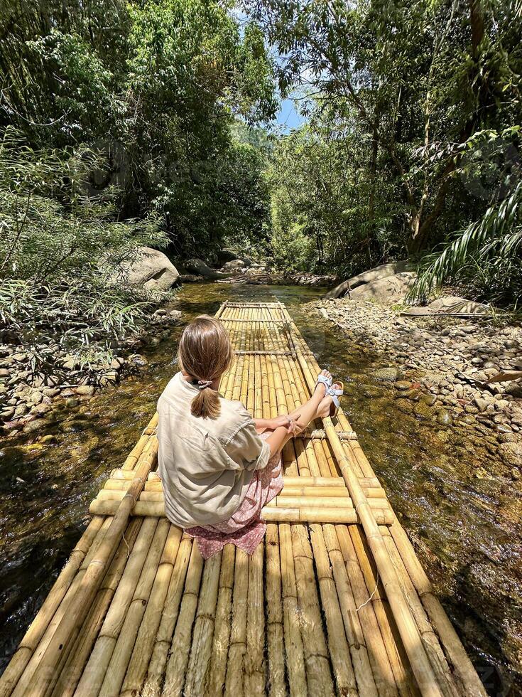 un niña suavemente flotadores abajo un pequeño río en un bambú balsa, inmerso en el tranquilidad de el rodeando selva paisaje foto