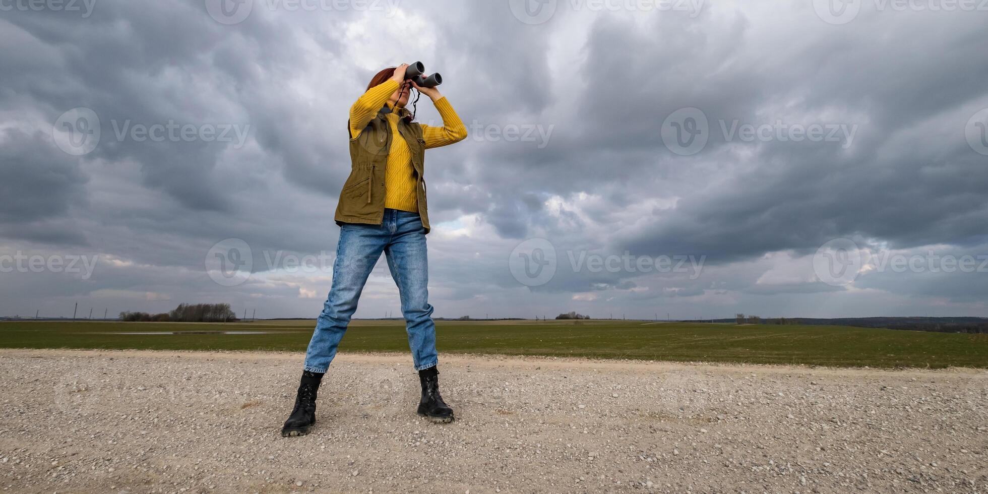 female ornithologist birdman or explorer watches birds with binoculars against a background of a stormy sky photo