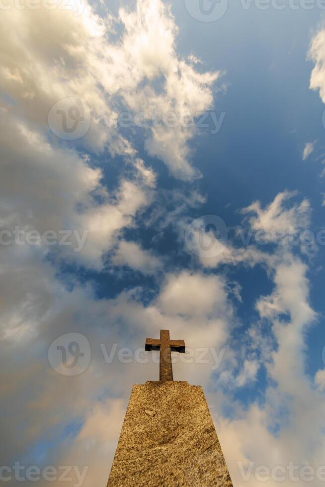 silhouette of stone grave cross against the background of a blue evening sky with clouds photo