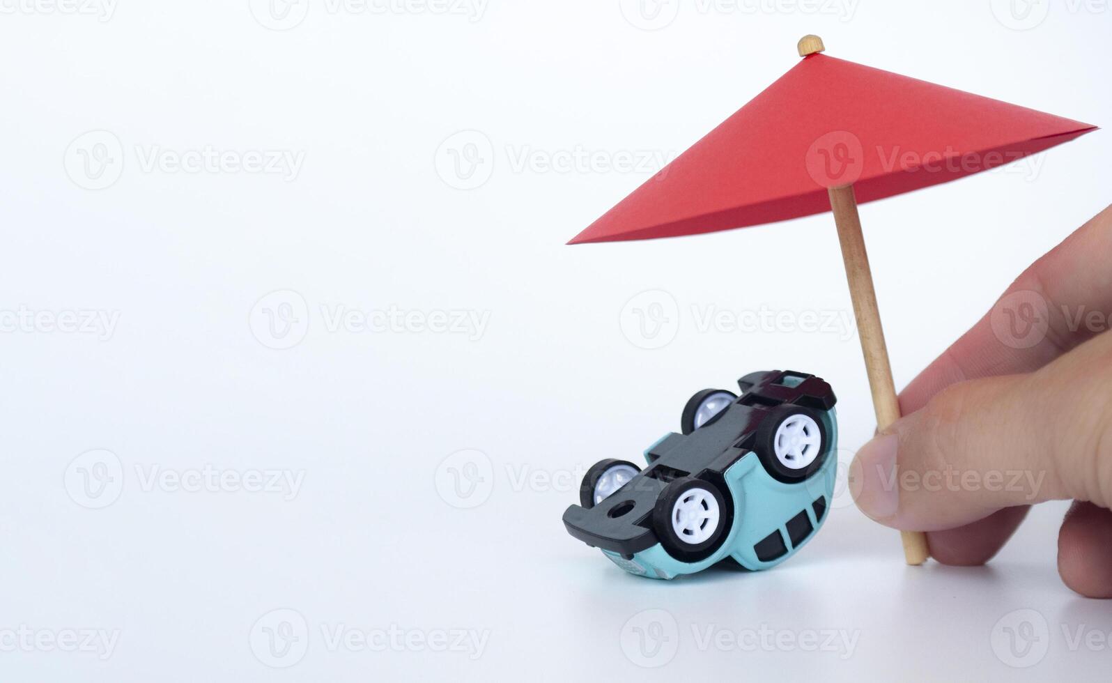 Hand holding red toy umbrella and upside down car on white background. Insurance coverage concept photo