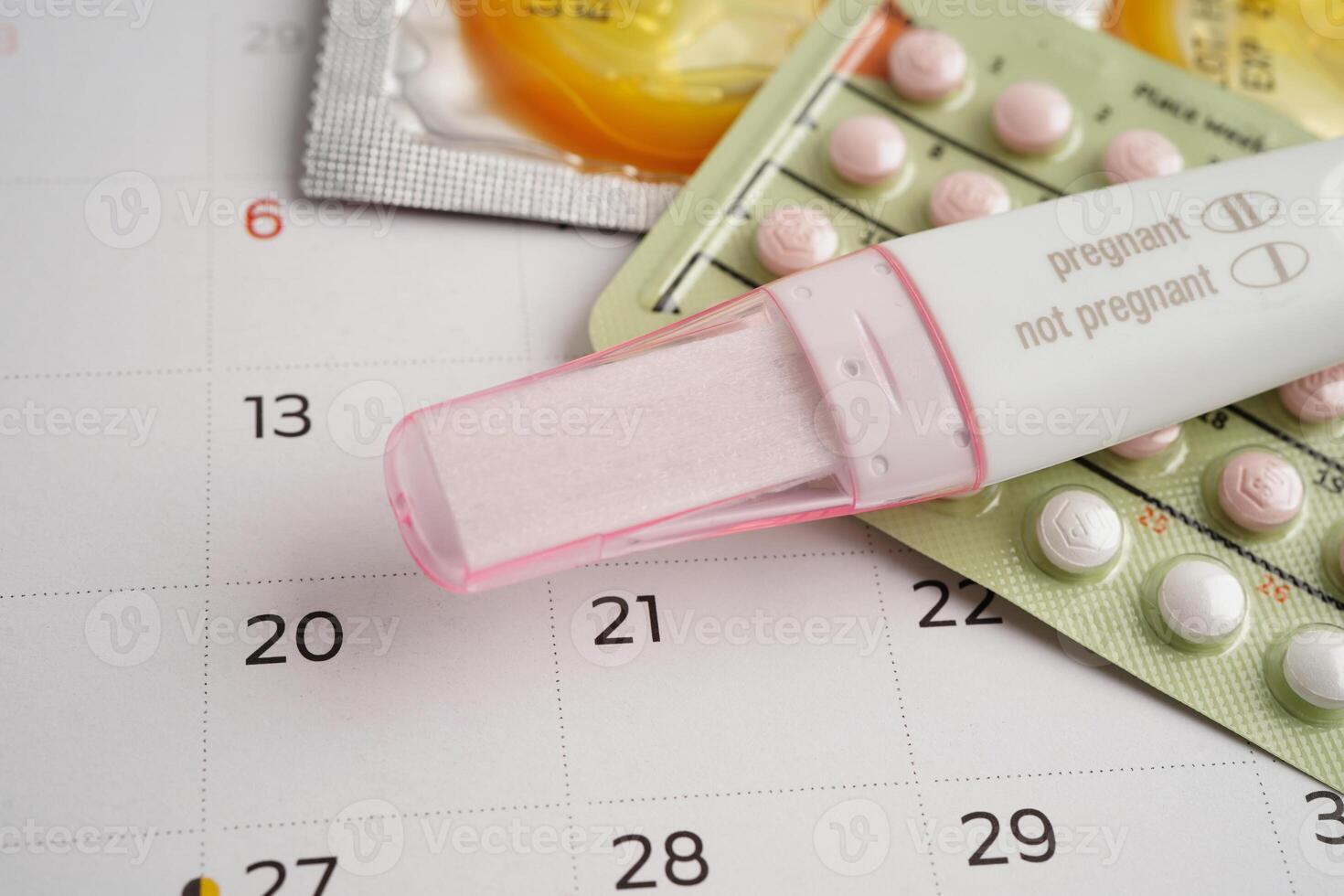 Pregnancy test with birth control pills and condom for female on calendar, ovulation day. photo