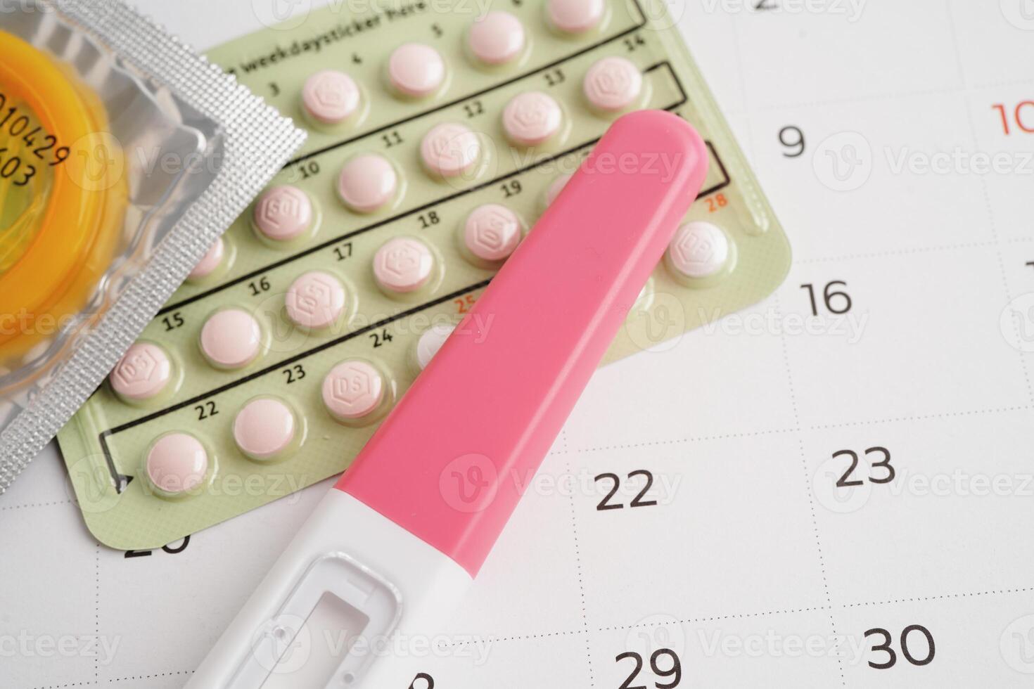 Pregnancy test with birth control pills and condom for female on calendar, ovulation day. photo