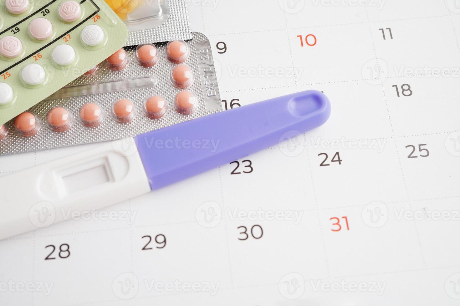 Pregnancy test with birth control pills and condom for female on calendar, ovulation day. photo