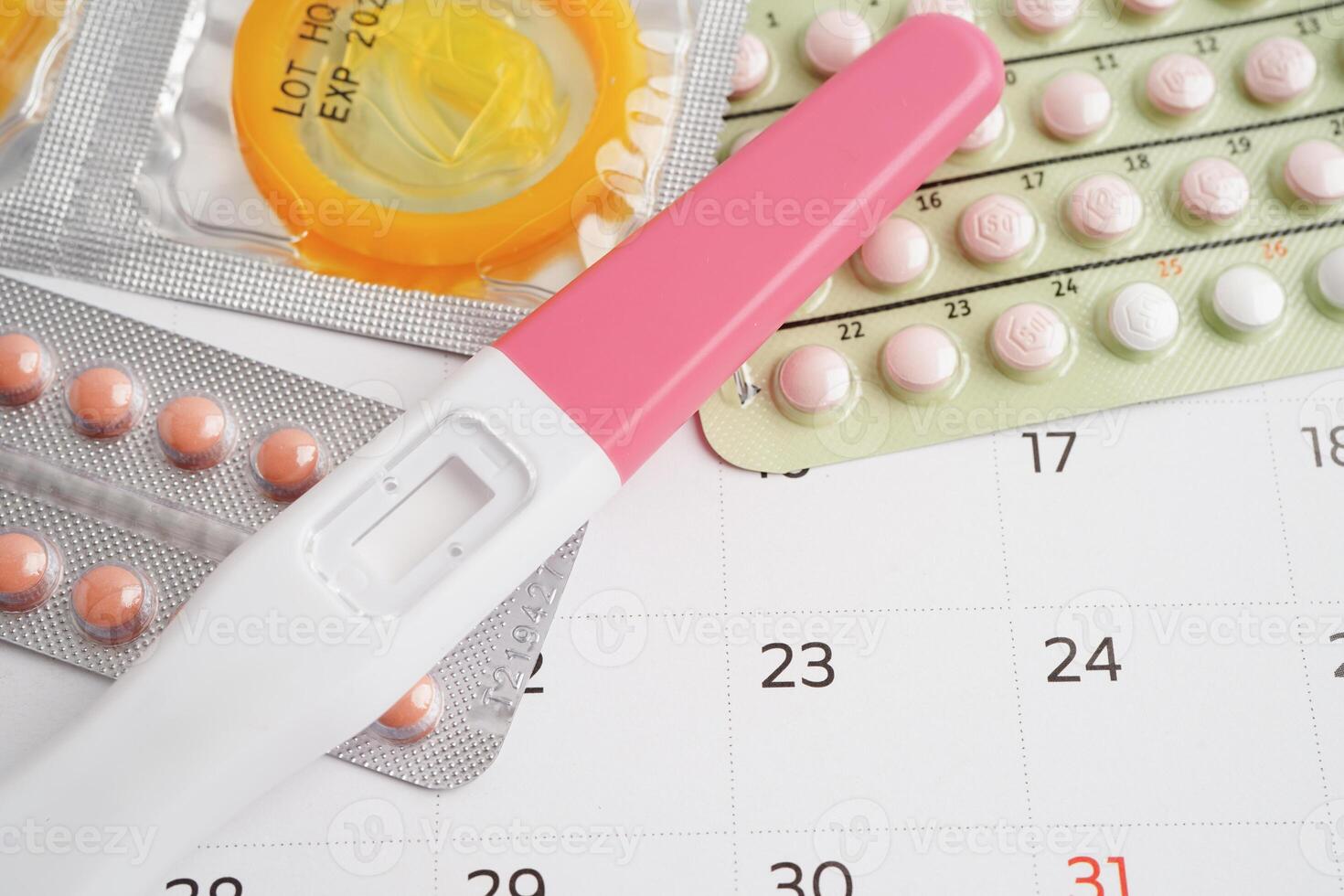 Pregnancy test with birth control pills and condom for female on calendar, ovulation day. photo