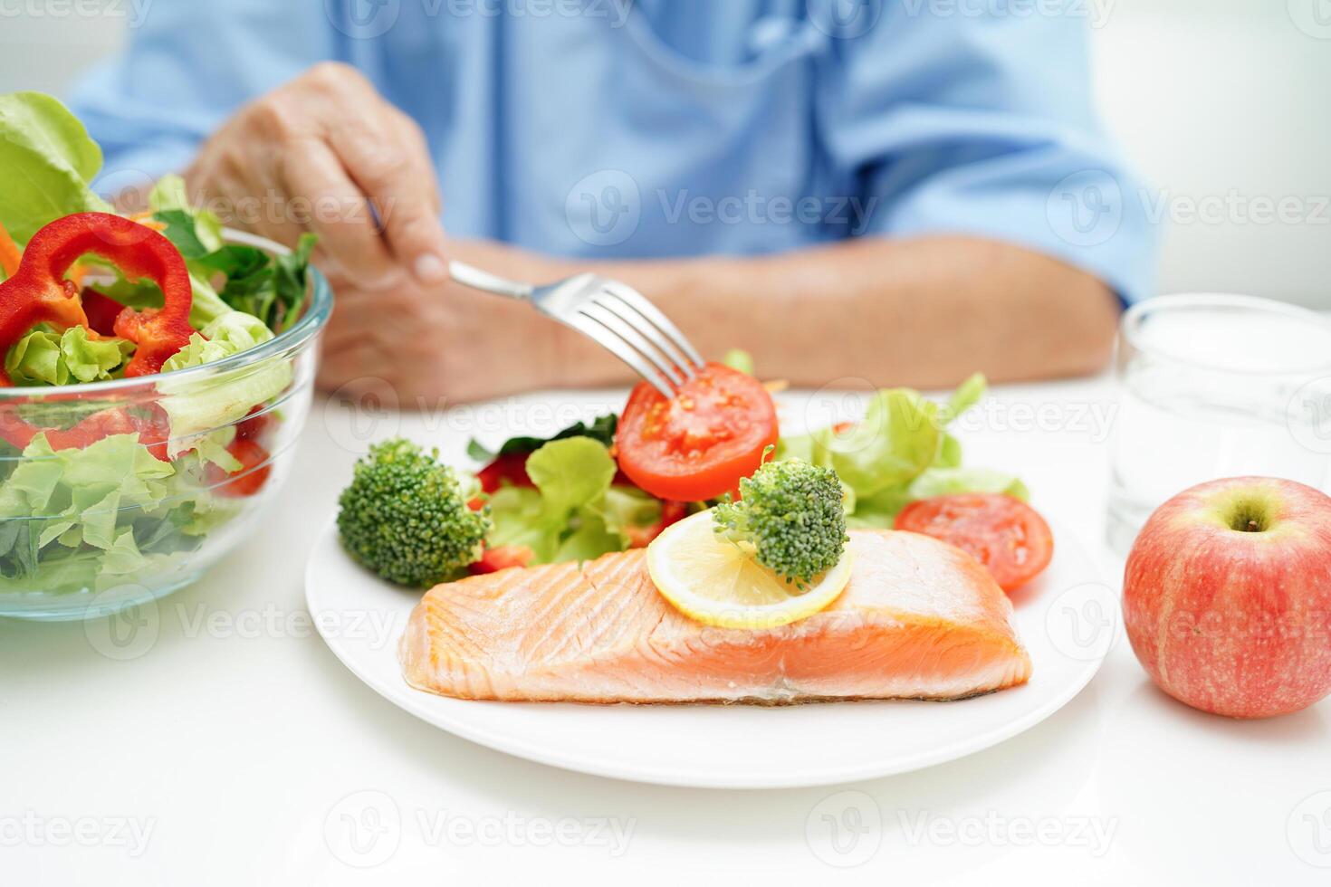 Asian elderly woman patient eating salmon stake and vegetable salad for healthy food in hospital. photo