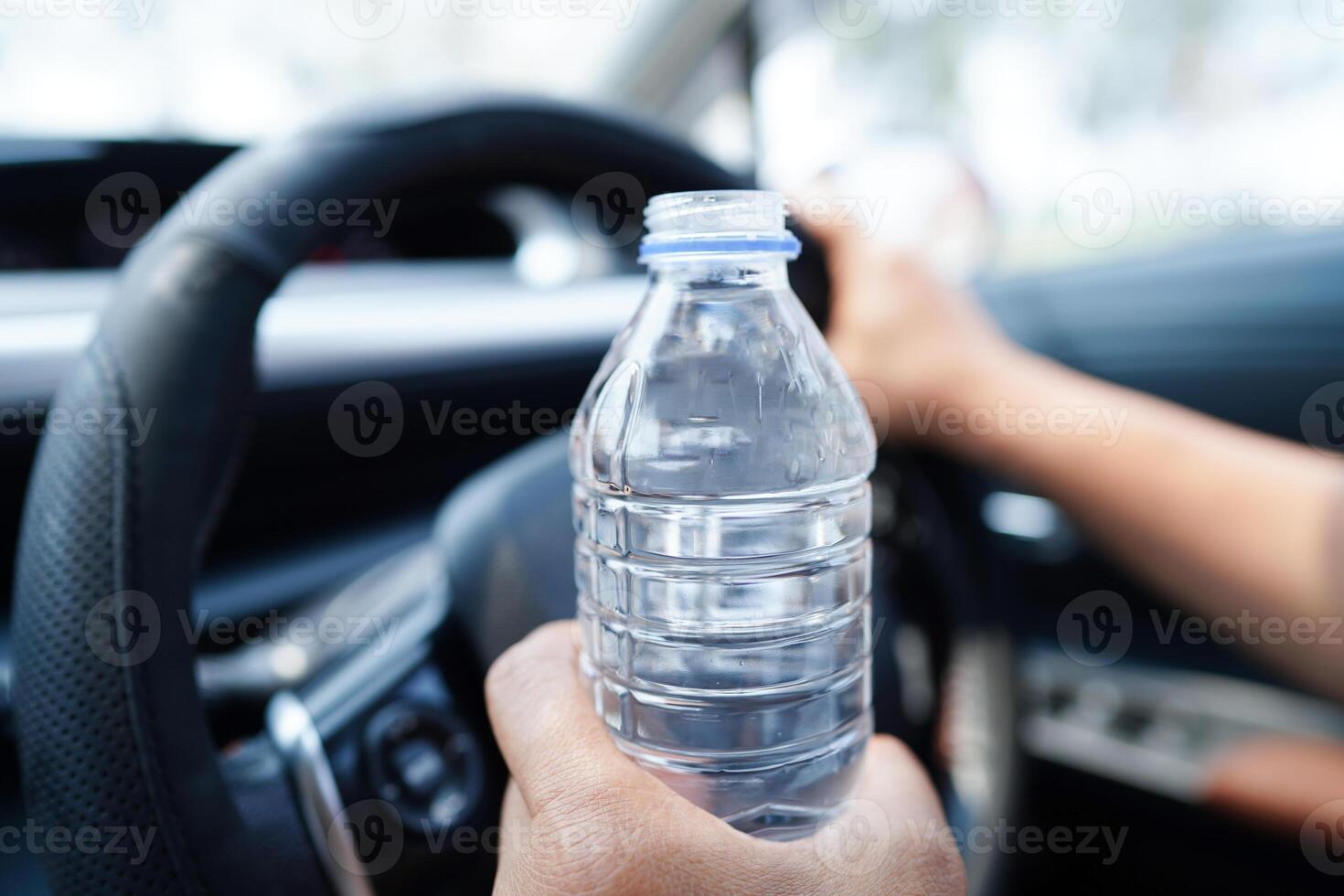 la conductora asiática sostiene agua fría para beber en el automóvil, es peligrosa y corre el riesgo de sufrir un accidente. foto