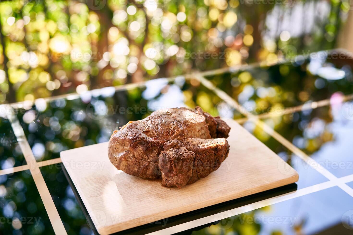 Baked roast beef lies on a cutting board on a mirror table on the balcony photo