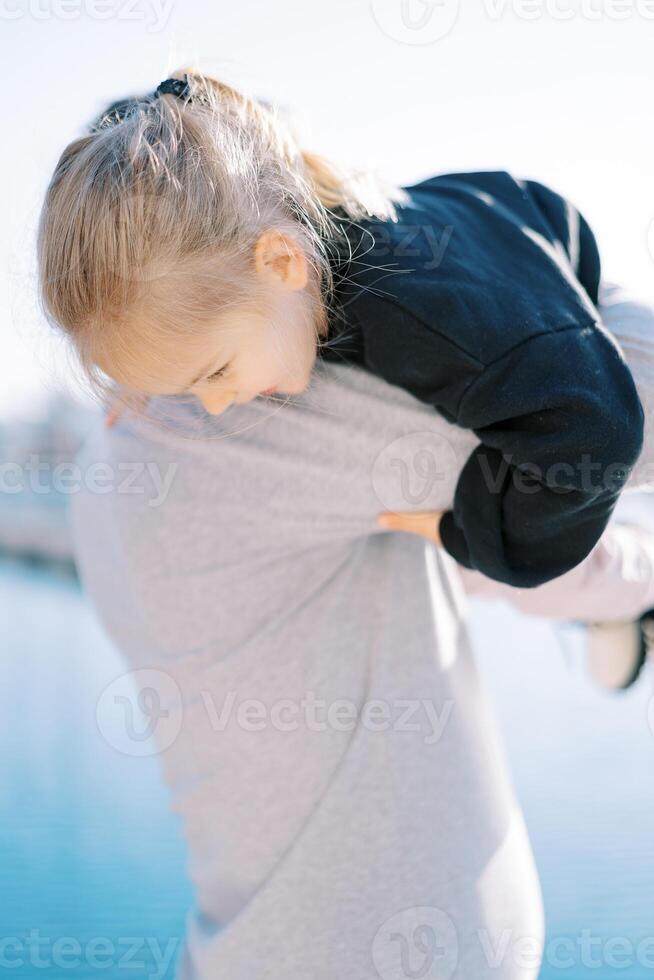 Dad lifts up the little girl holding onto his shoulder. Back view photo