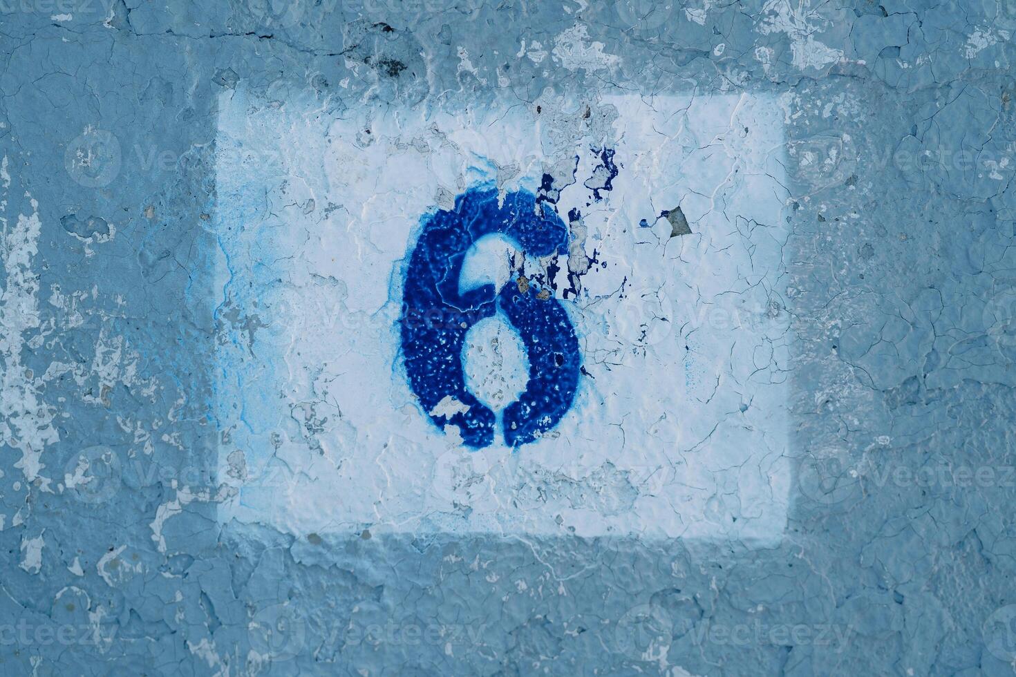 Number six painted on a blue scratched wall in a rectangle with peeling paint photo