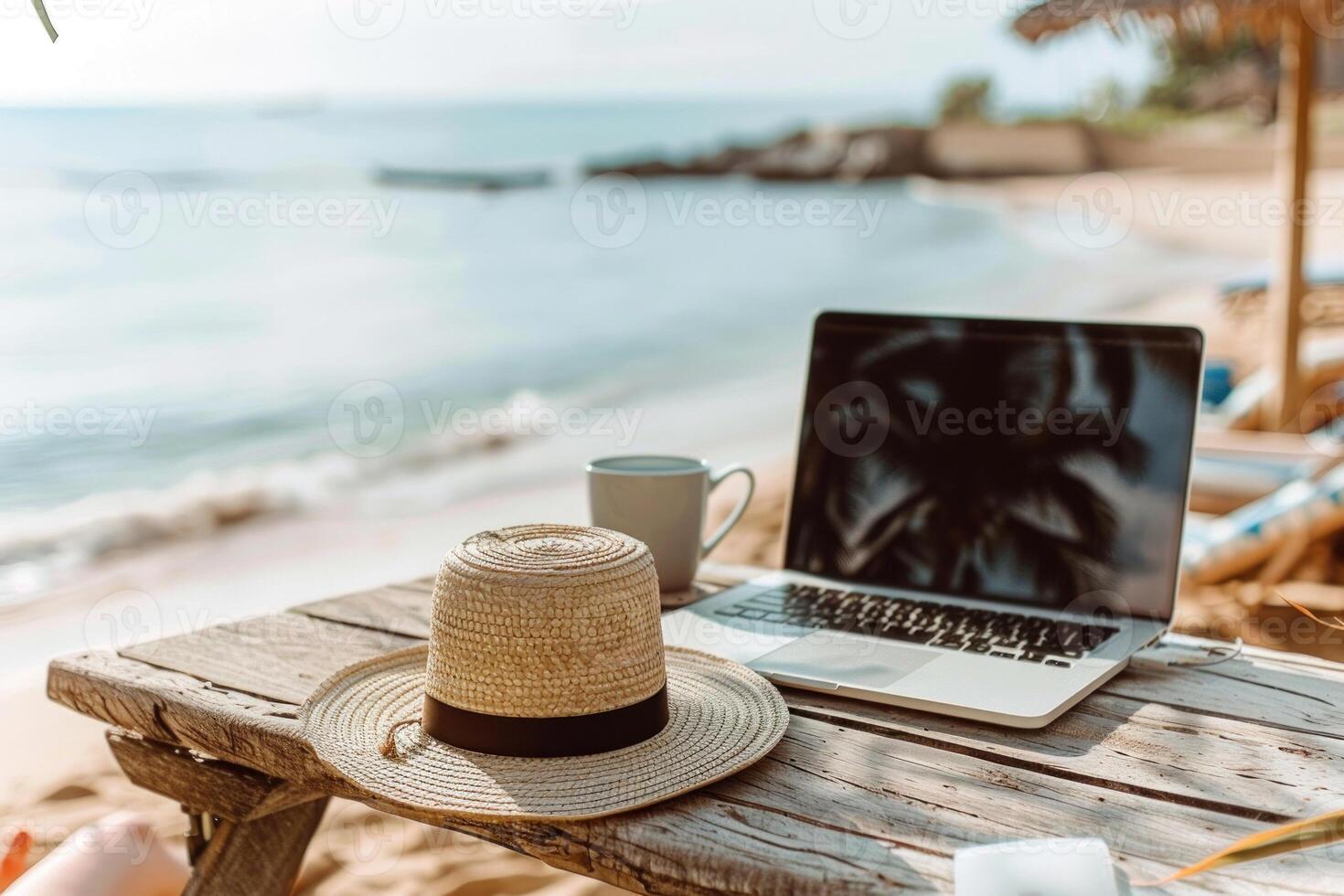 A laptop is open on a table next to a straw hat and a cup photo