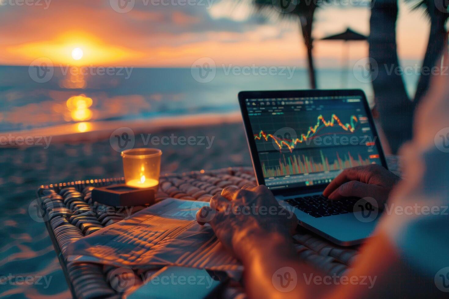 A person is sitting on a beach with a laptop open, working on a financial report photo