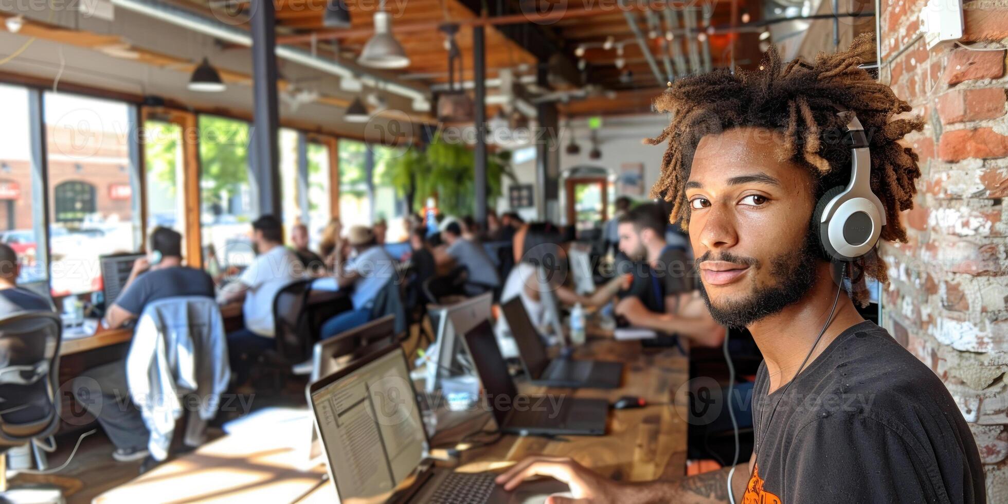 A man with dreadlocks is sitting at a desk in a room with other people photo
