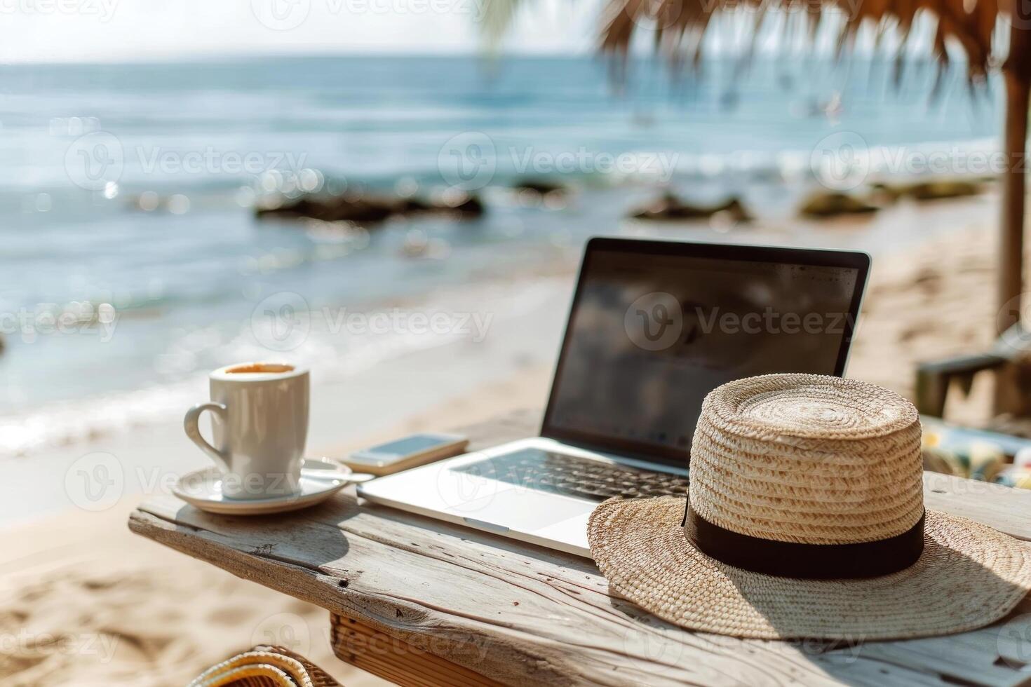 A laptop is open on a table next to a straw hat and a cup photo