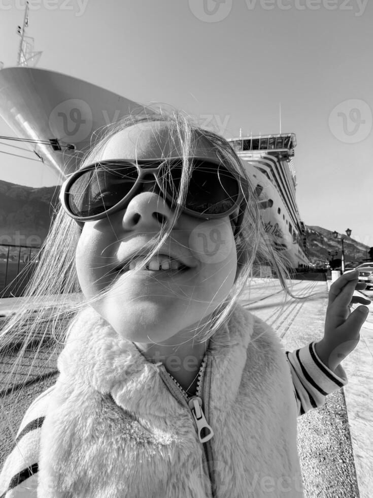 Little girl in sunglasses on the background of a large boat. Black and white photo