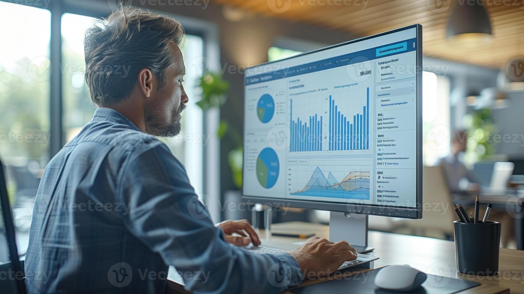 A man is sitting at a desk in front of a computer monitor, working on a project photo