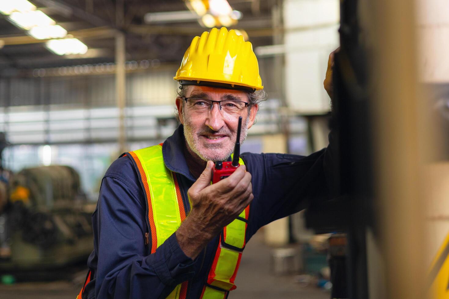 man wearing a yellow hard hat and safety vest is holding a walkie talkie photo