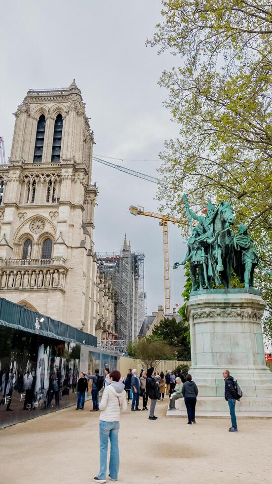Tourists exploring the historic Notre Dame Cathedral with ongoing reconstruction, next to a statue in Paris, France, captured on April 14th, 2024, reflecting cultural heritage and travel photo