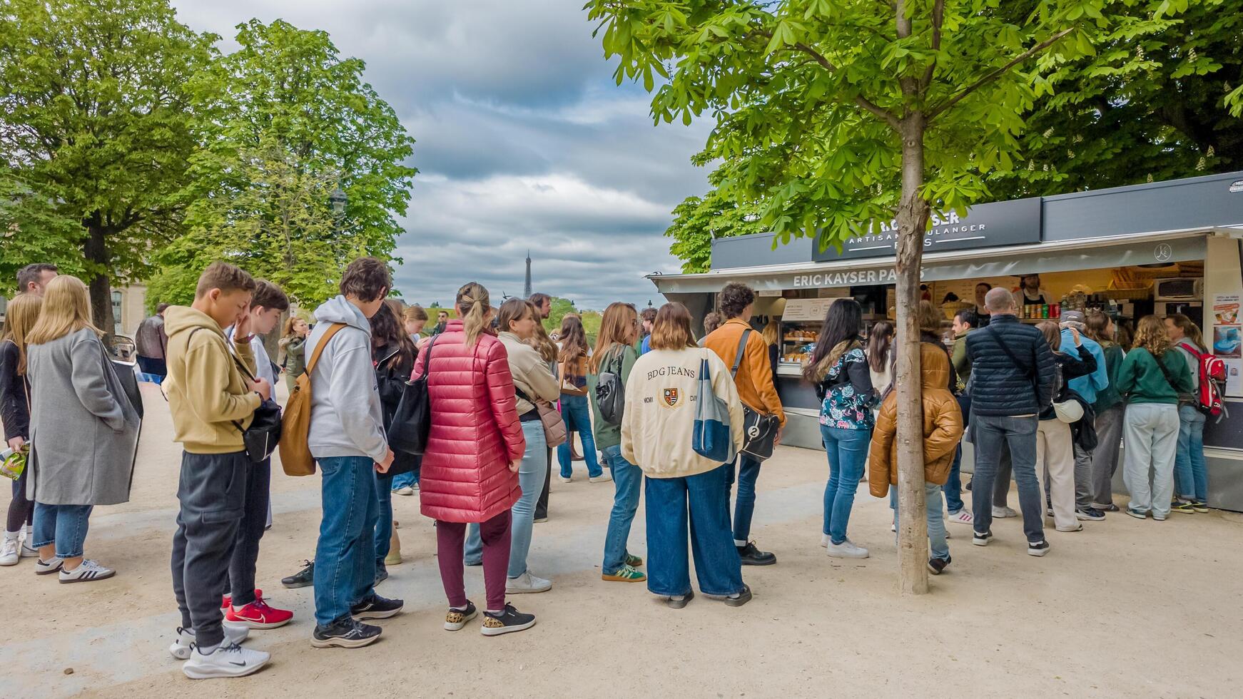 Diverse group of people queuing at an outdoor snack kiosk under a cloudy sky in Paris, France, related to tourism and daily life, captured on April 14th, 2024 photo