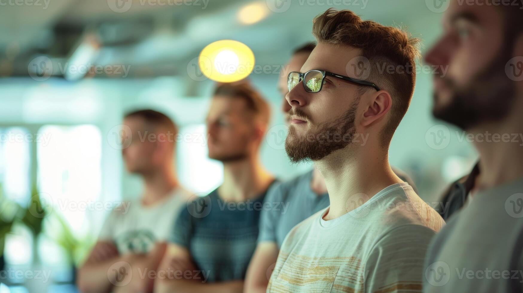 A group of men standing in a brightly lit room attentively listening to a presentation about male skincare photo