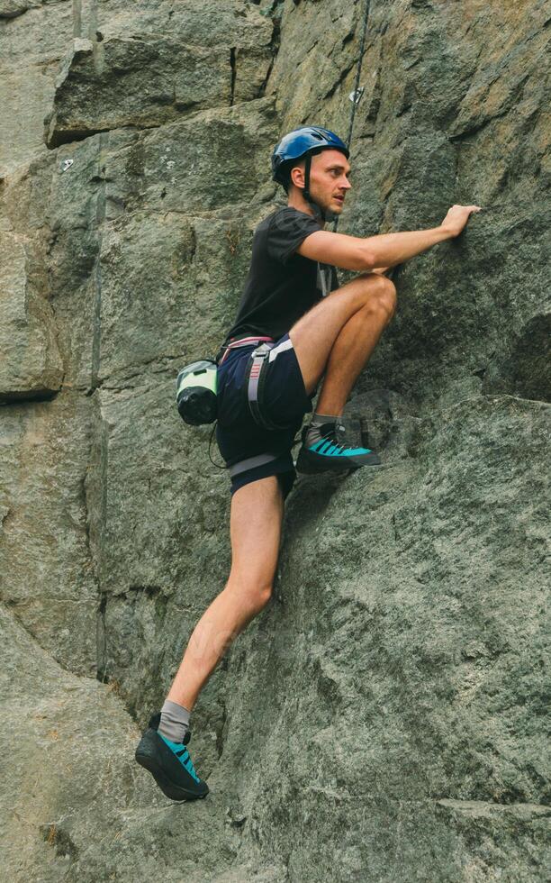 Young man in equipment doing rock climbing outdoors. Training area for outdoor activities. Extreme sport. photo