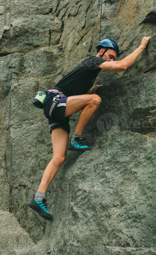 Young man in equipment doing rock climbing outdoors. Training area for outdoor activities. Extreme sport. photo