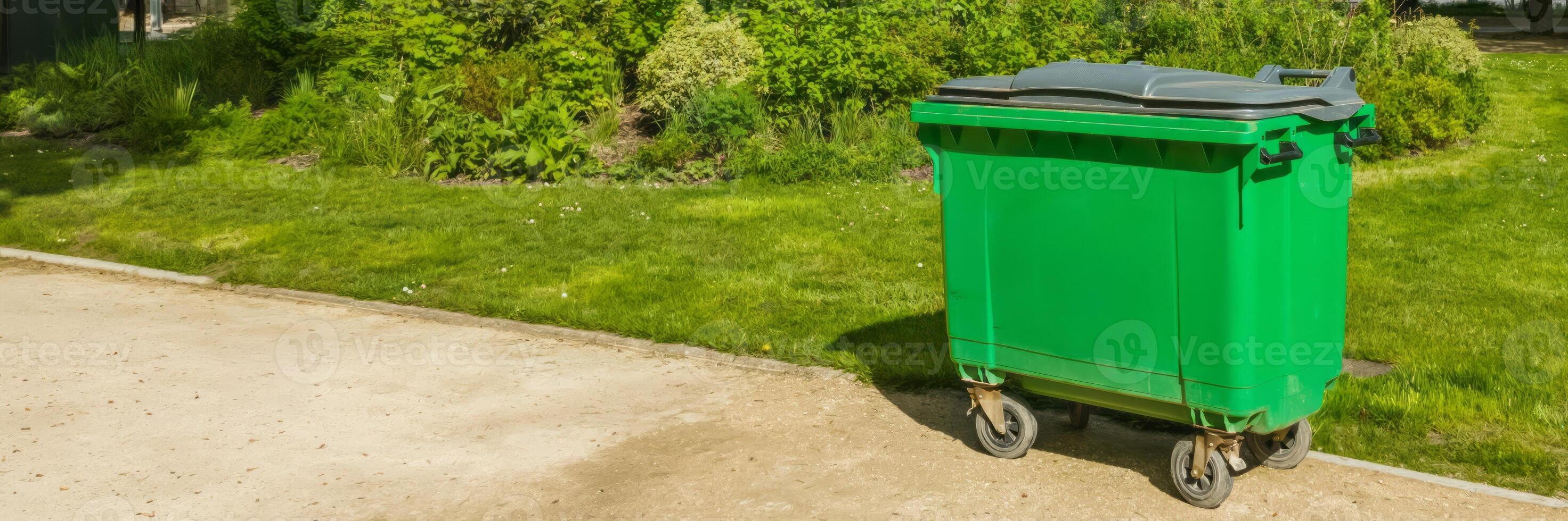 Large green waste container on wheels placed beside a footpath in a public park, symbolizing urban cleanliness and environmental awareness, related to Earth Day photo