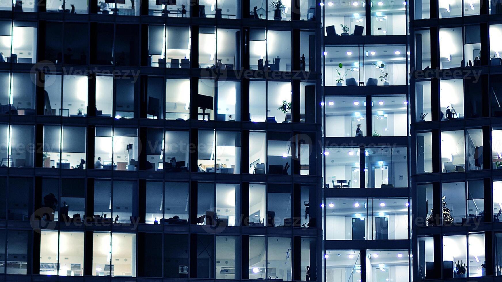 Fragment of the glass facade of a modern corporate building at night. Modern glass office in city. Big glowing windows in modern office buildings at night, in rows of windows light shines. photo