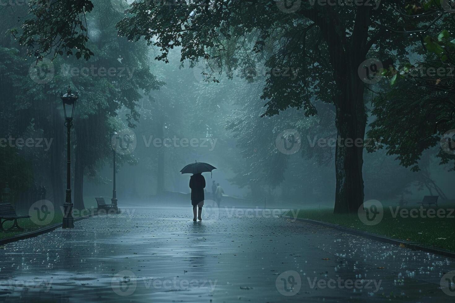 Lonely figure with an umbrella walking through a heavily rain soaked park, mist and drizzle around photo