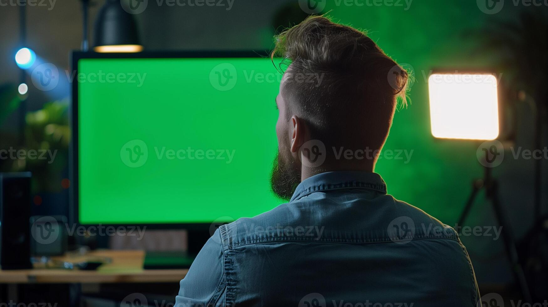 Bearded man working on post production with green screen monitor in a dimly lit personal studio, related to film editing, technology, and International Workers Day photo