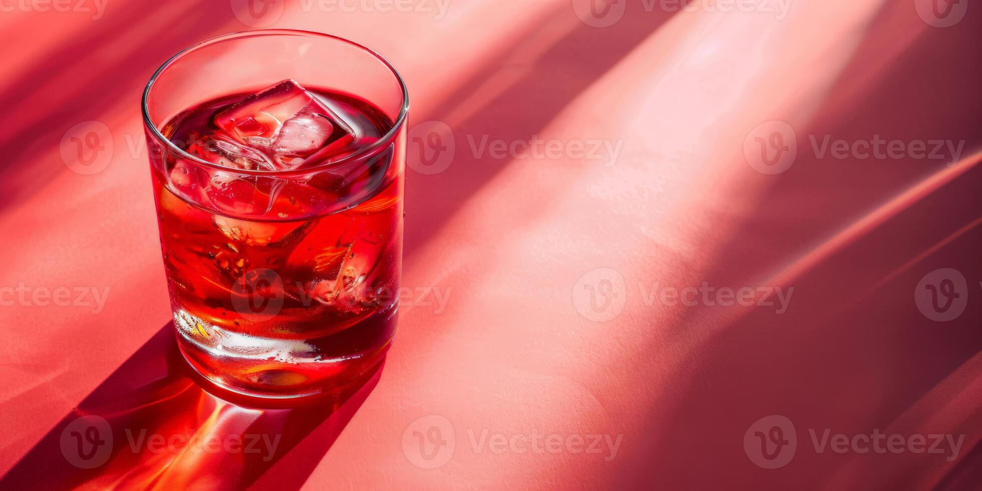 Iced red cocktail in a clear glass set against a vibrant pink surface, invoking concepts of summer refreshments and celebratory toasts photo