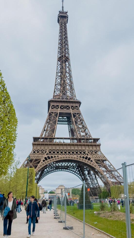 visitantes vagante cerca el icónico eiffel torre en un nublado primavera día en París, Francia, capturar el esencia de viaje y europeo puntos de referencia en abril 14, 2024 foto