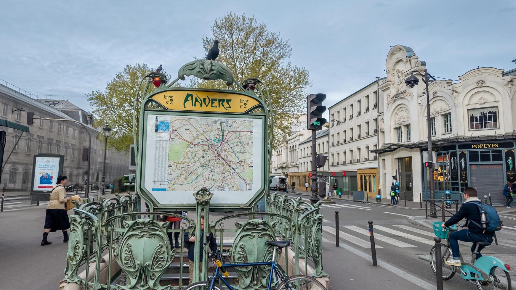 Spring day at a traditional Art Nouveau metro station in Paris, France, with pedestrians and cyclists, captured on April 14th, 2024, related to urban travel photo