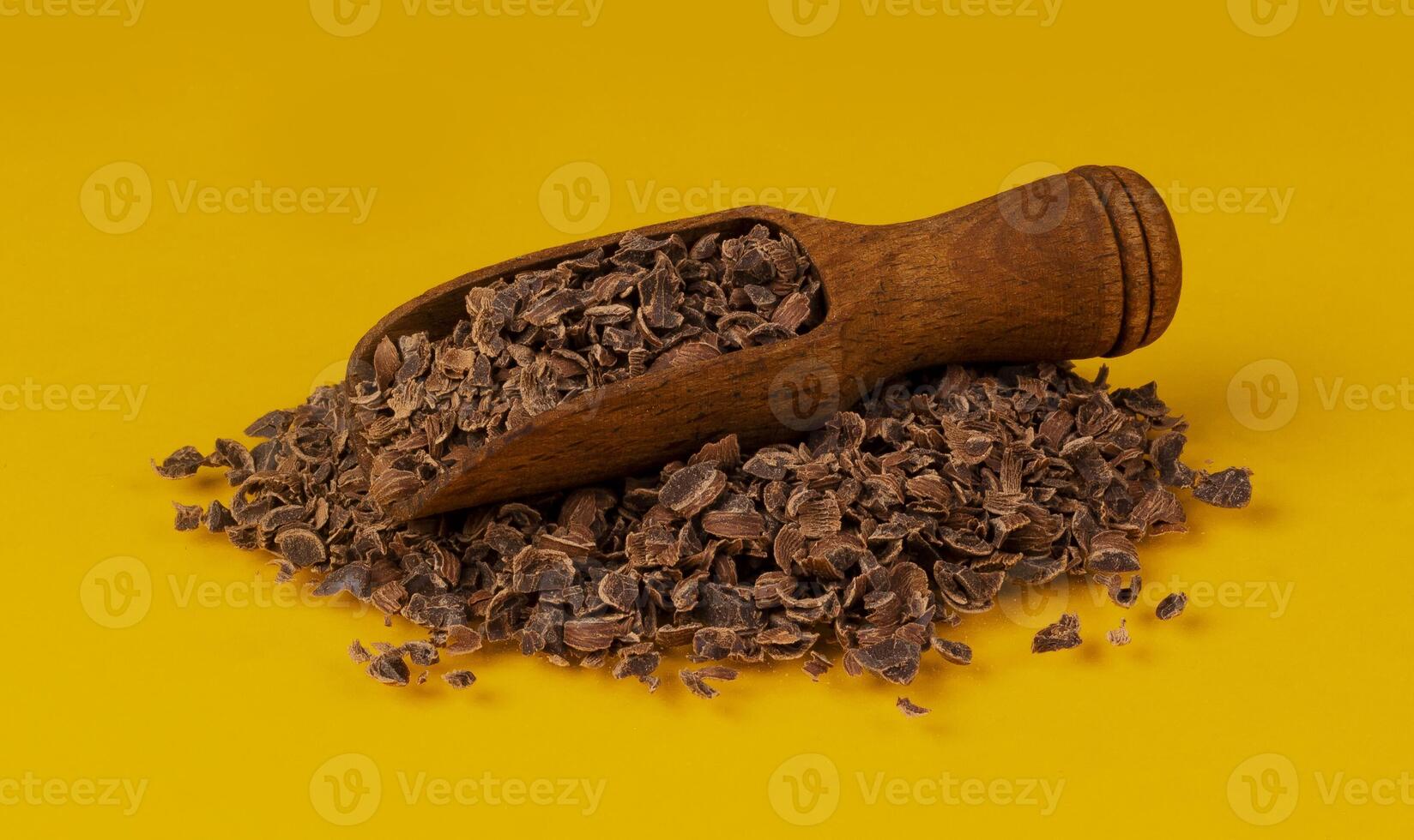 Grated chocolate. Pile of ground chocolate in wooden scoop isolated on yellow color background, closeup photo