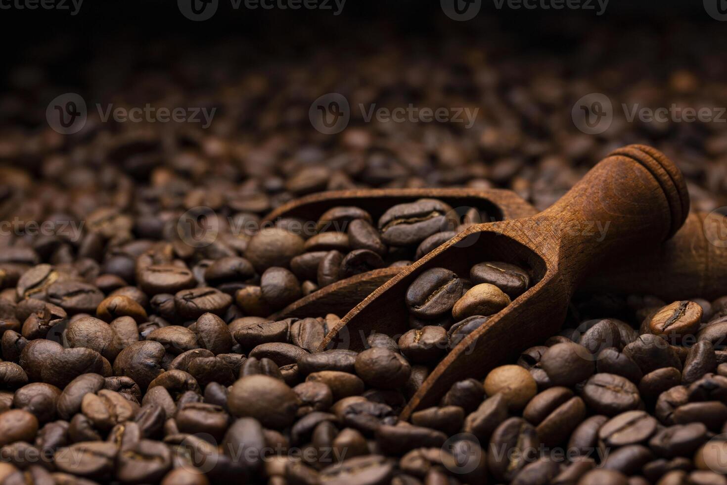 Pile of coffee beans with wooden scoop, close up, dark background with copy space, shallow depth of field photo
